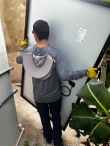 Trabajador sosteniendo un panel solar mientras camina por el pasillo de una casa para subirla por una escalera de mano para la instalación en el techo.