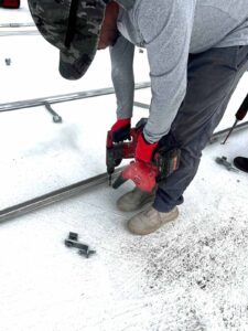 Un trabajador utilizando una taladradora eléctrica para instalar el andamiaje de las placas solares.