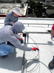 Dos instaladores trabajando en el cableado de un sistema de paneles solares en el techo de una casa.