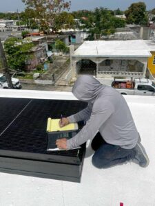 Técnico anotando medidas y datos en una libreta junto a paneles o placas solares en el techo de una casa.