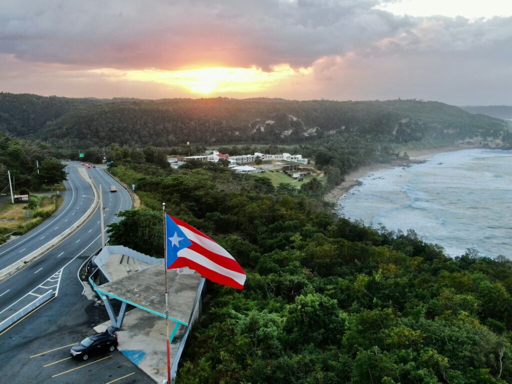 Toma aérea de la bandera de Puerto Rico ondeando en el aire durante un atardecer dorado en Quebradillas