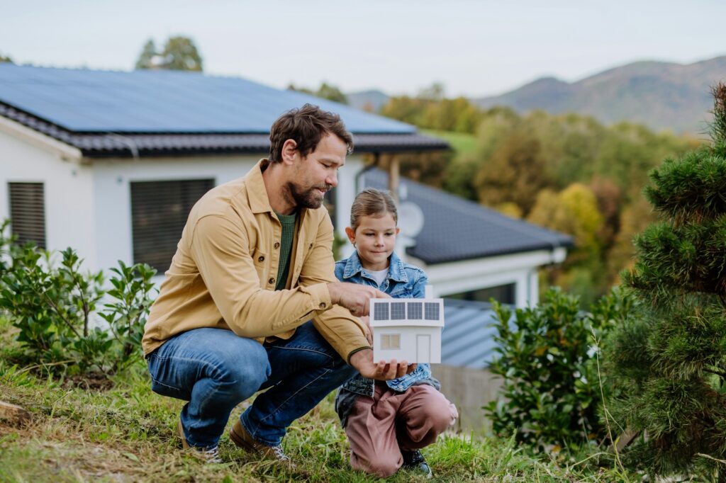 Little girl with her dad holding paper model of house with solar panels, explaining how it works