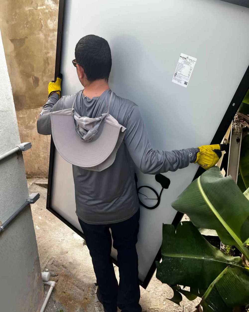 Trabajador sosteniendo un panel solar mientras camina por el pasillo de una casa para subirla por una escalera de mano para la instalación en el techo.