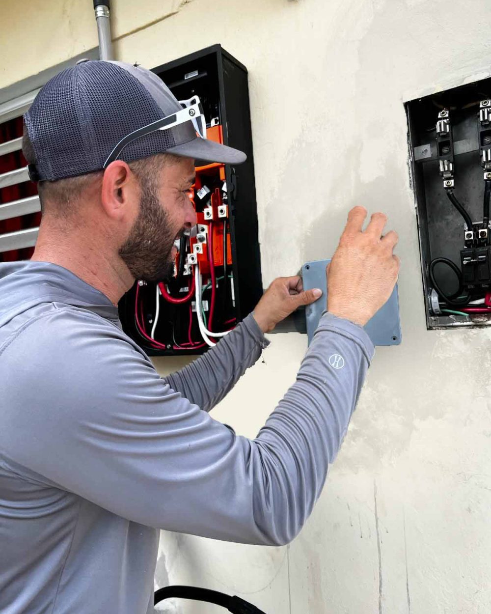 Un electricista sonriendo mientras instala o conecta componentes eléctricos en un sistema de baterías Tesla en una vivienda.